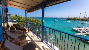A balcony with lounge chairs, a view of the sea with boats, and a clear sky.