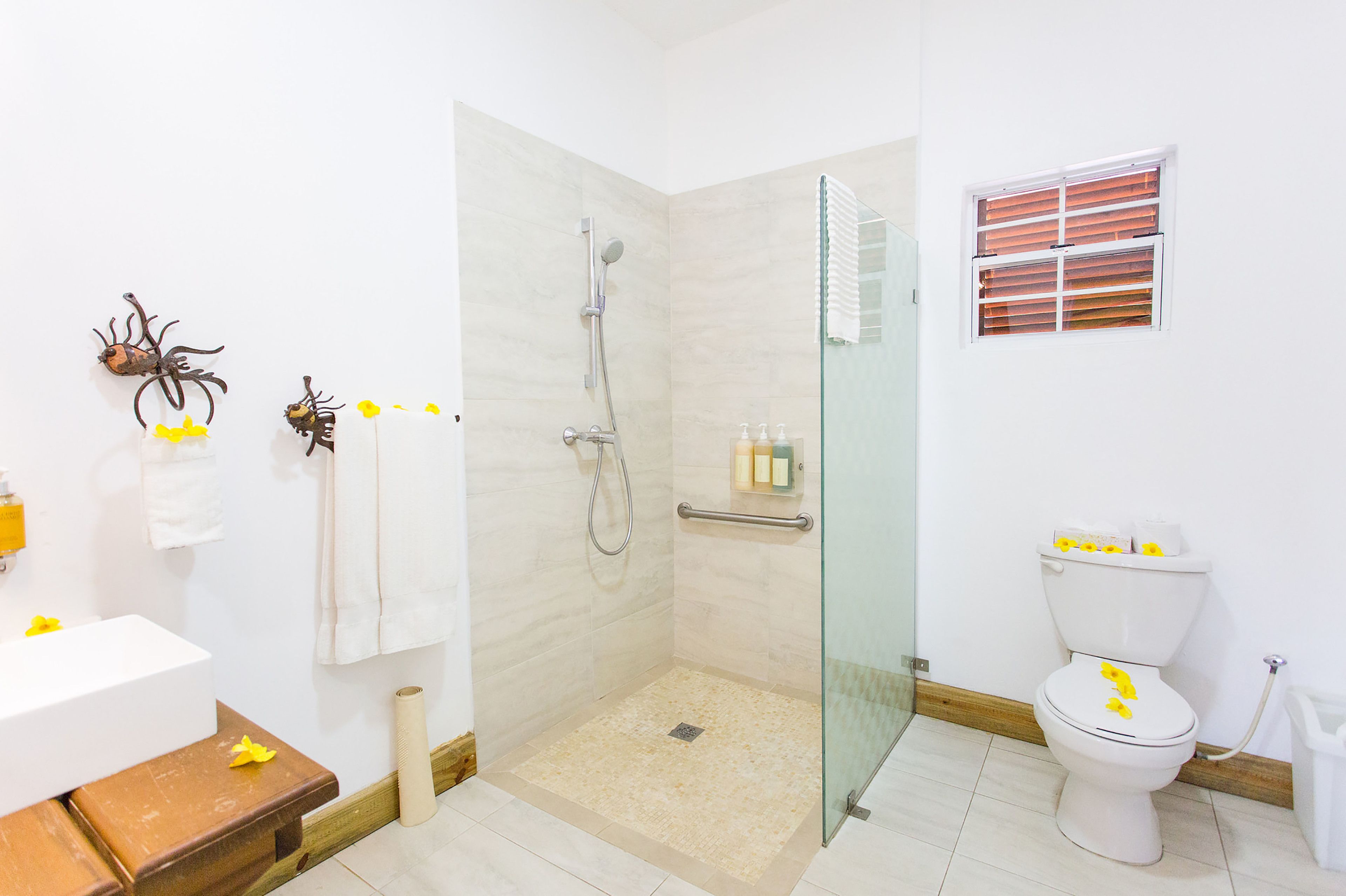 A bathroom with a glass-enclosed shower, a white toilet, and a sink with a wooden stool.
