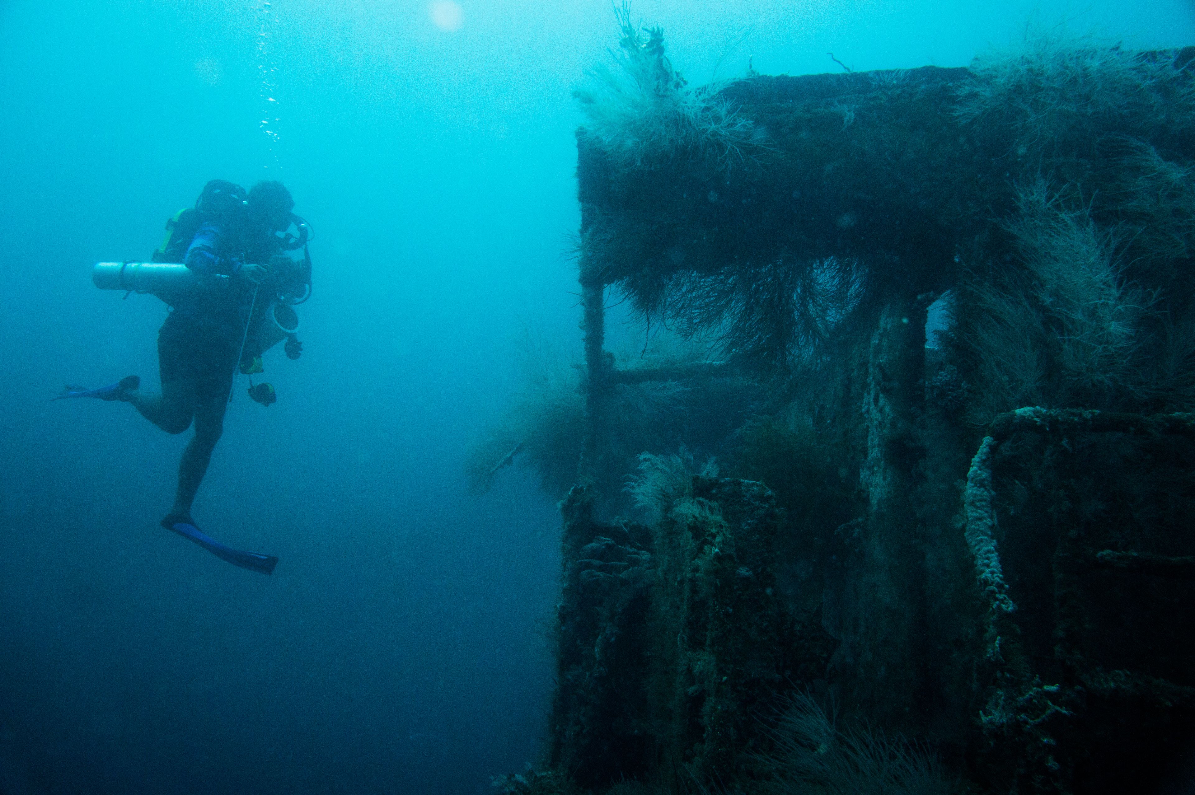 Un buceador explora un sitio submarino con estructuras visibles y crecimiento marino.