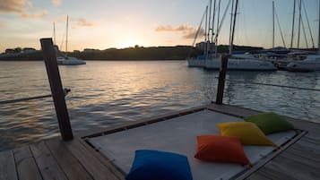 Une terrasse en bois avec un espace détente agrémenté d’un revêtement en treillis blanc et d’une rangée de coussins colorés.