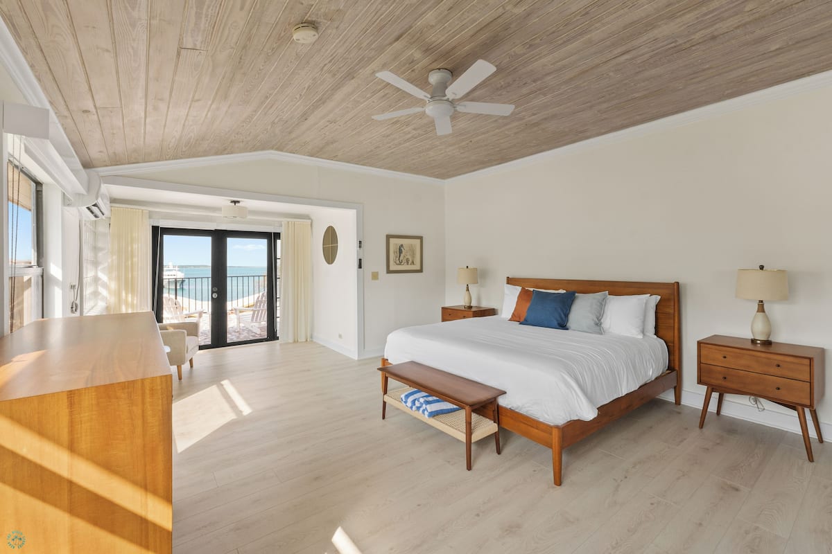 A spacious bedroom with a large bed, wooden headboard, bedside tables, and a ceiling fan.