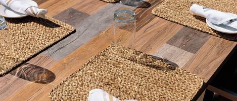 A wooden dining table with woven placemats, neatly folded white napkins, and clear glass water glasses.