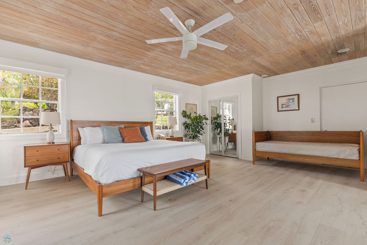 A bedroom with a wooden ceiling, a bed, a bench, and a desk.