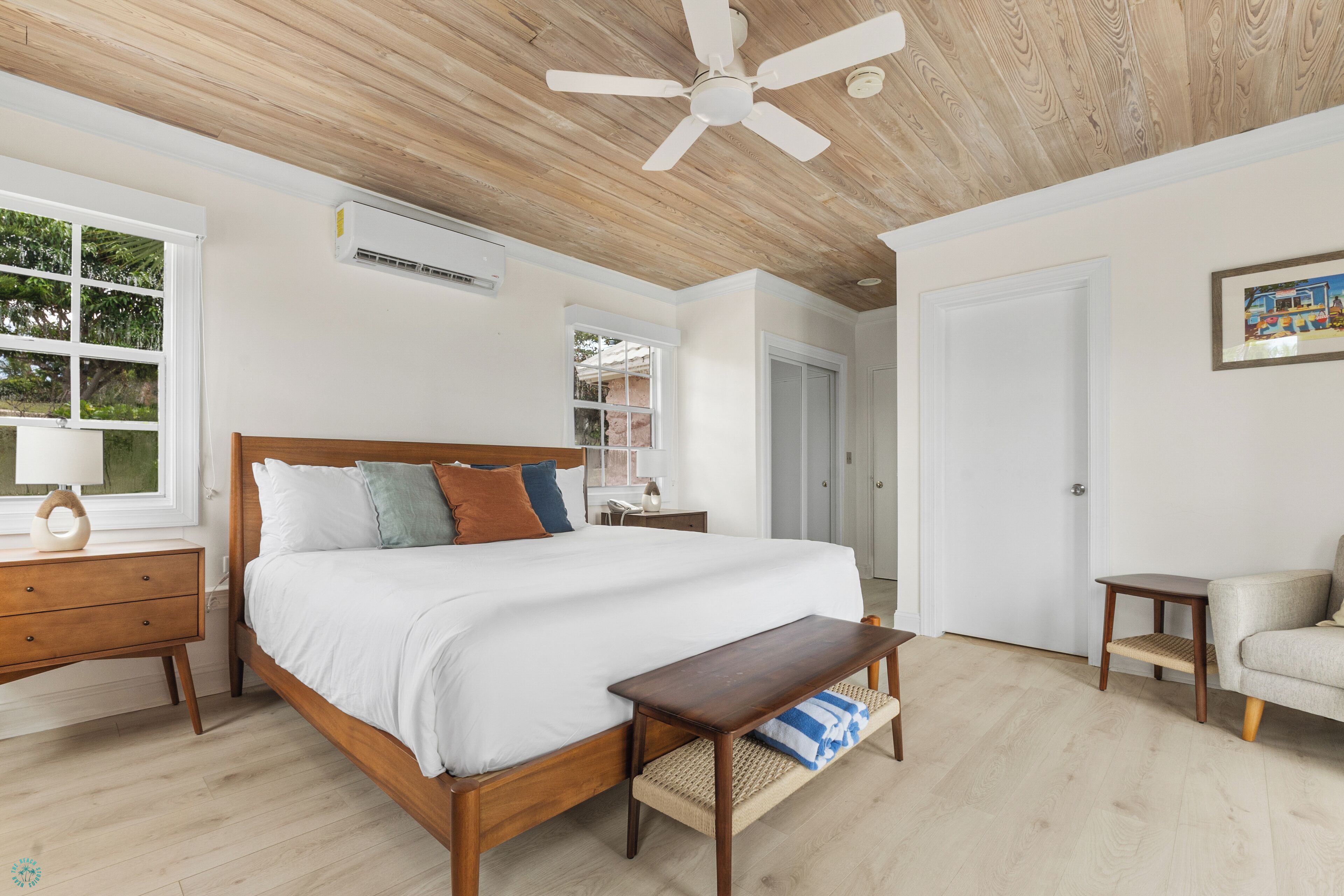 Une chambre à coucher avec un lit en bois, un ventilateur de plafond, une table de chevet, un banc et une fenêtre avec des stores.