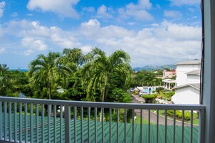 A view from a balcony with a green roof, palm trees, and a clear blue sky.