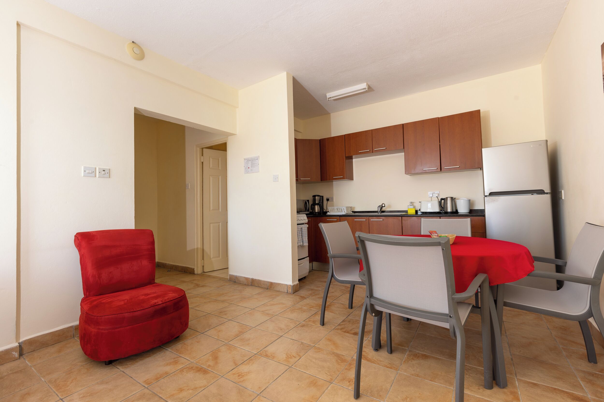 A compact kitchen with wooden cabinets, a stainless steel refrigerator, and a dining area with a red tablecloth.
