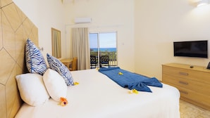 A hotel room with a bed, a TV, a wooden headboard, a balcony with a view, and a TV on a wooden dresser. - Siesta Hotel (St. George's)