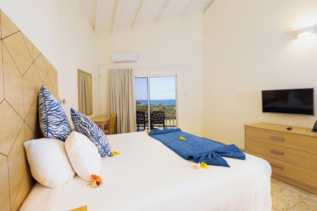 A hotel room with a bed, a TV, a wooden headboard, a balcony with a view, and a TV on a wooden dresser.