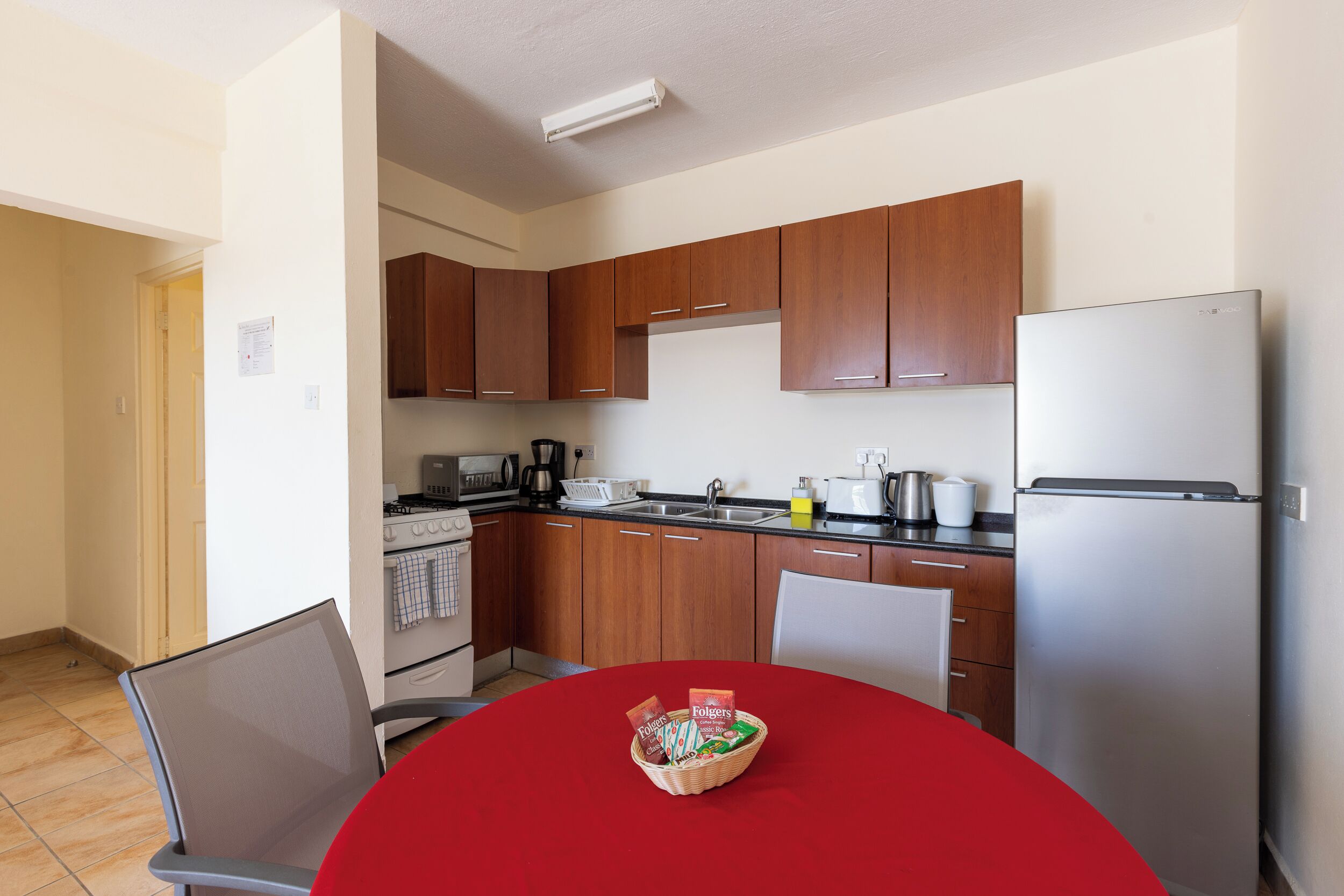 A compact kitchen with wooden cabinets, a stainless steel refrigerator, and a dining table with a red tablecloth.