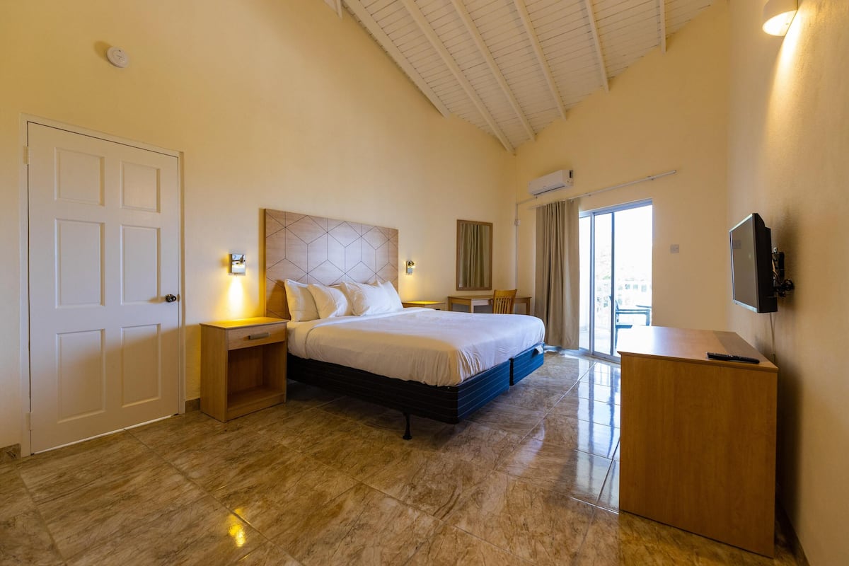 A bedroom with a bed, bedside tables, a desk, a television, and a sliding glass door to a balcony.