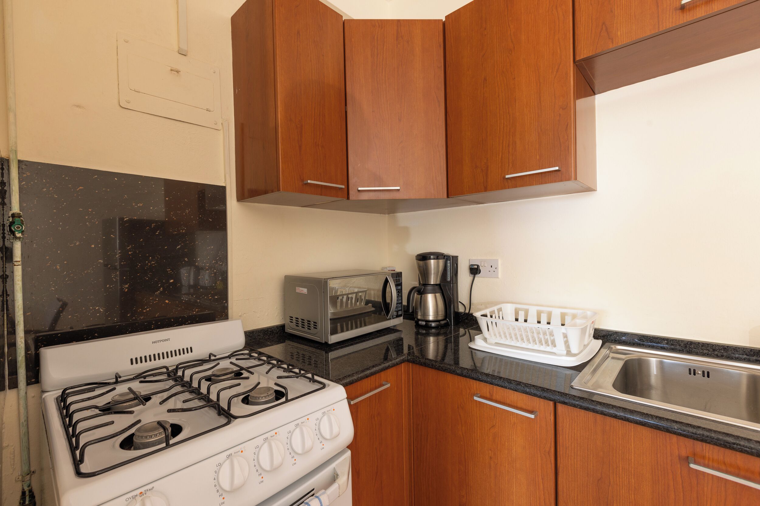 Una cocina compacta con armarios de madera, estufa a gas, microondas y cafetera.