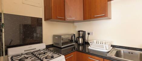 Una cocina compacta con armarios de madera, estufa a gas, microondas y cafetera.
