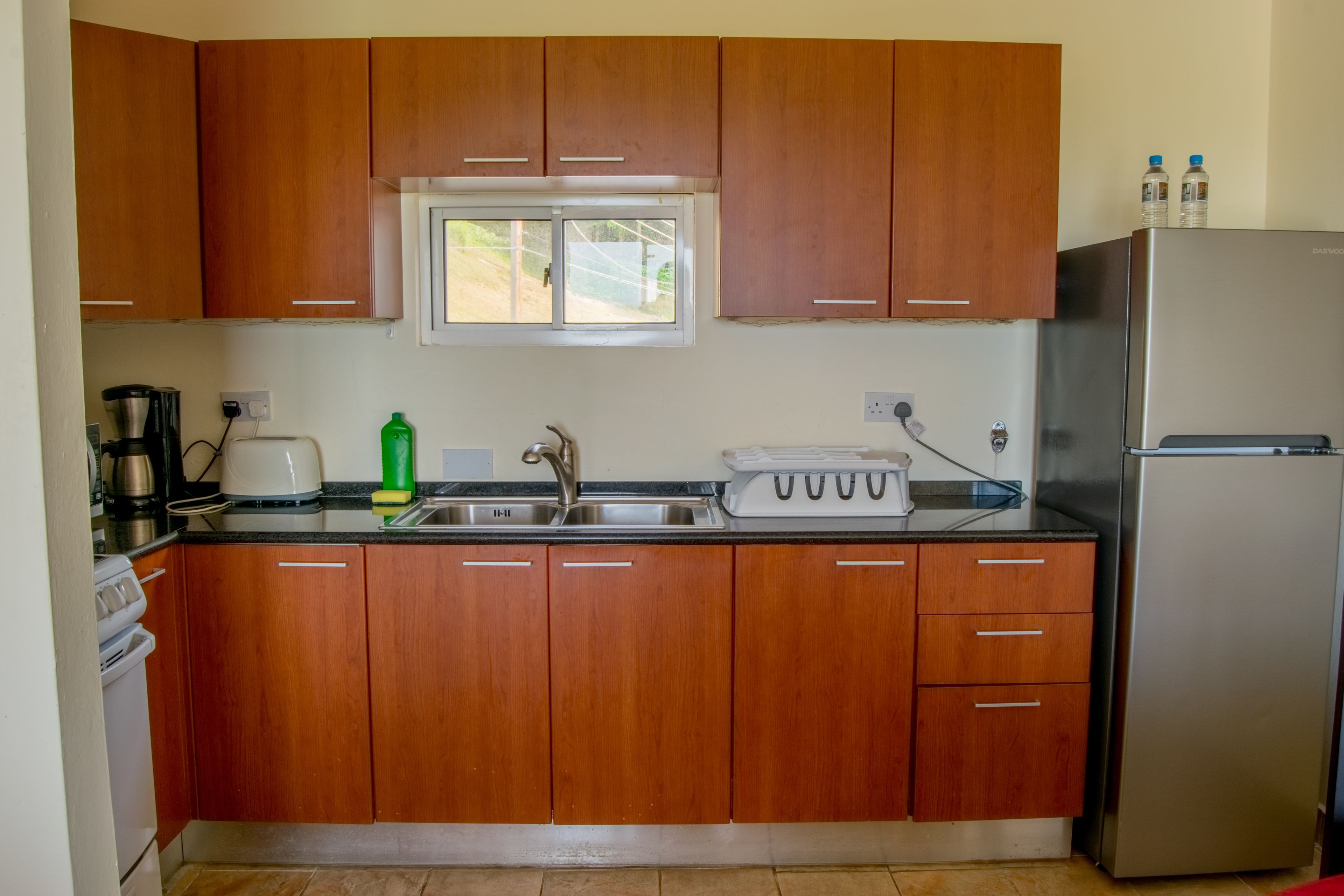 Una cocina con armarios de madera, un refrigerador de acero inoxidable, una ventana y un lavamanos.