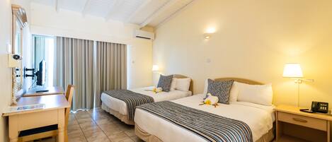 Camera d'albergo con due letti, una scrivania, una sedia, un comodino con una lampada e una finestra con tende.