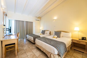 Habitación de hotel con dos camas, un escritorio, una silla, una mesita de noche con lámpara y una ventana con cortinas.