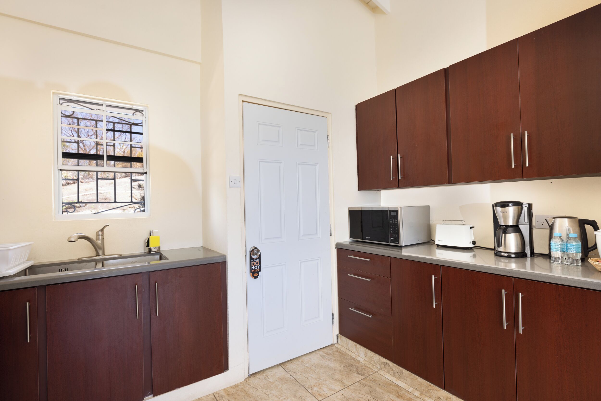 A kitchen with a white door, stainless steel sink, and wooden cabinets.
