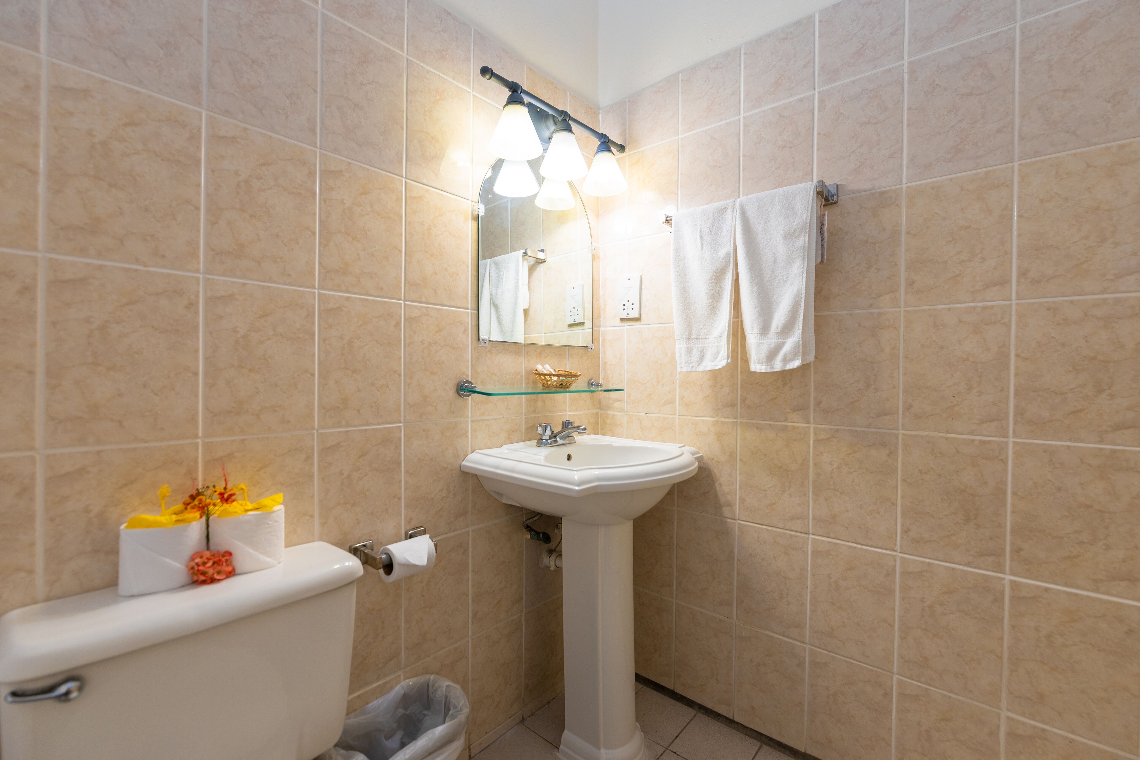 Un baño con baldosas color crema, un lavamanos blanco, un espejo y un perchero para toallas.