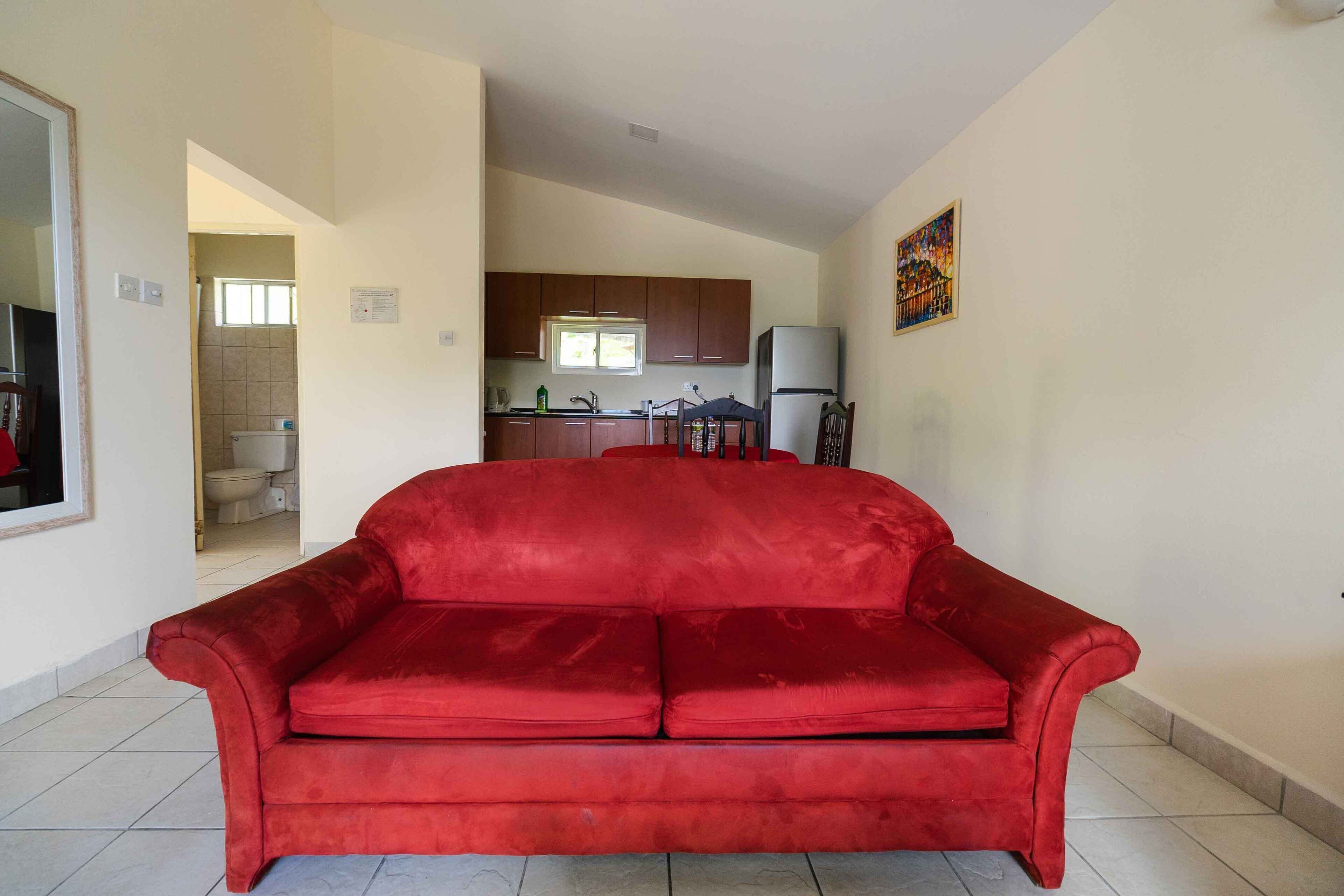 Um sofá vermelho numa sala de estar, com uma cozinha ao fundo.