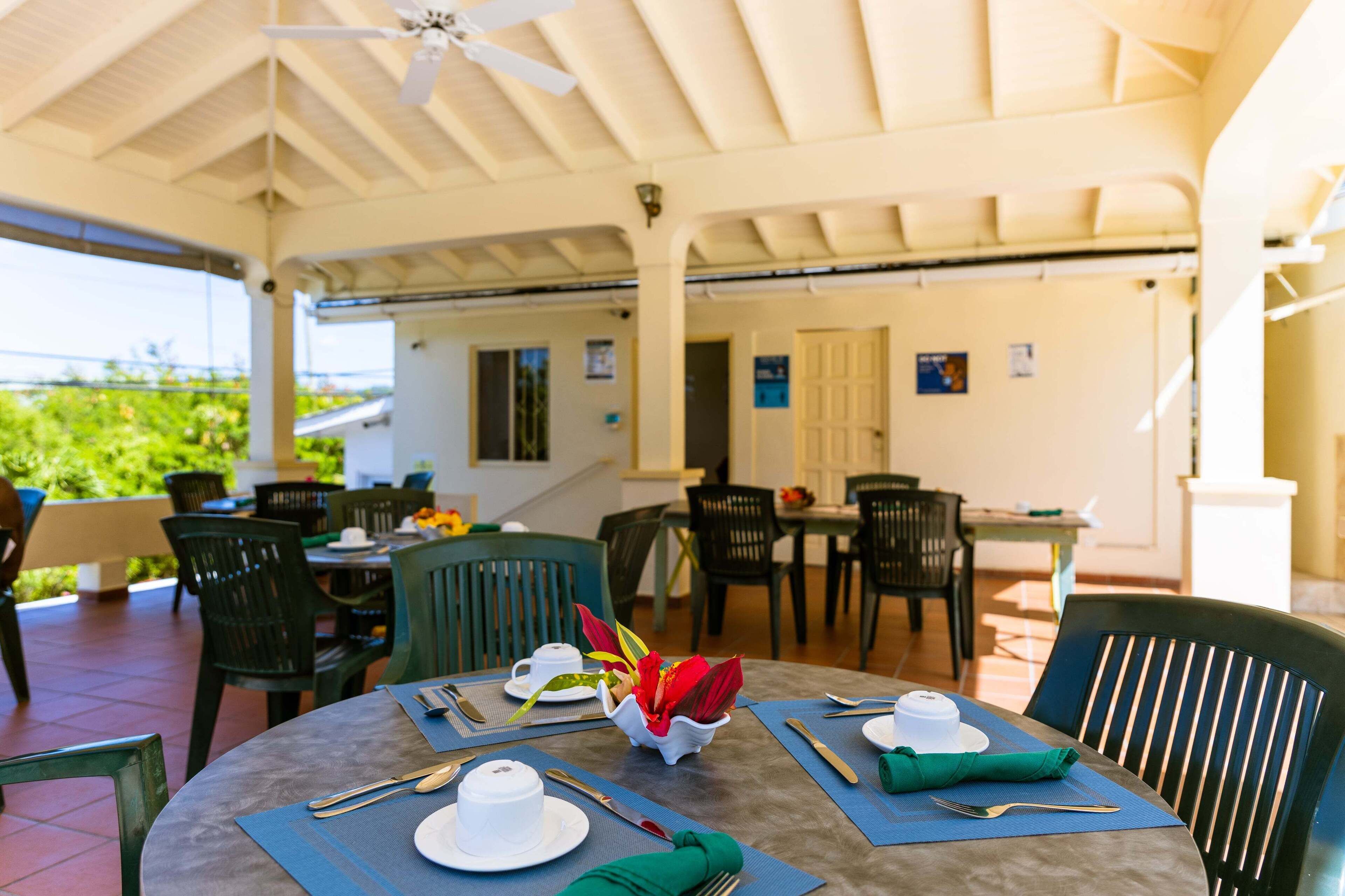 A covered outdoor dining area with tables set for two, chairs, and a ceiling fan.