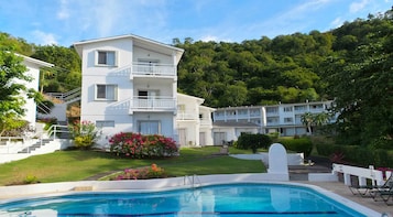 A multi-story hotel with a swimming pool, surrounded by lush greenery and a hillside.