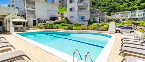 A swimming pool with lounge chairs, a restaurant, and a parking area.
