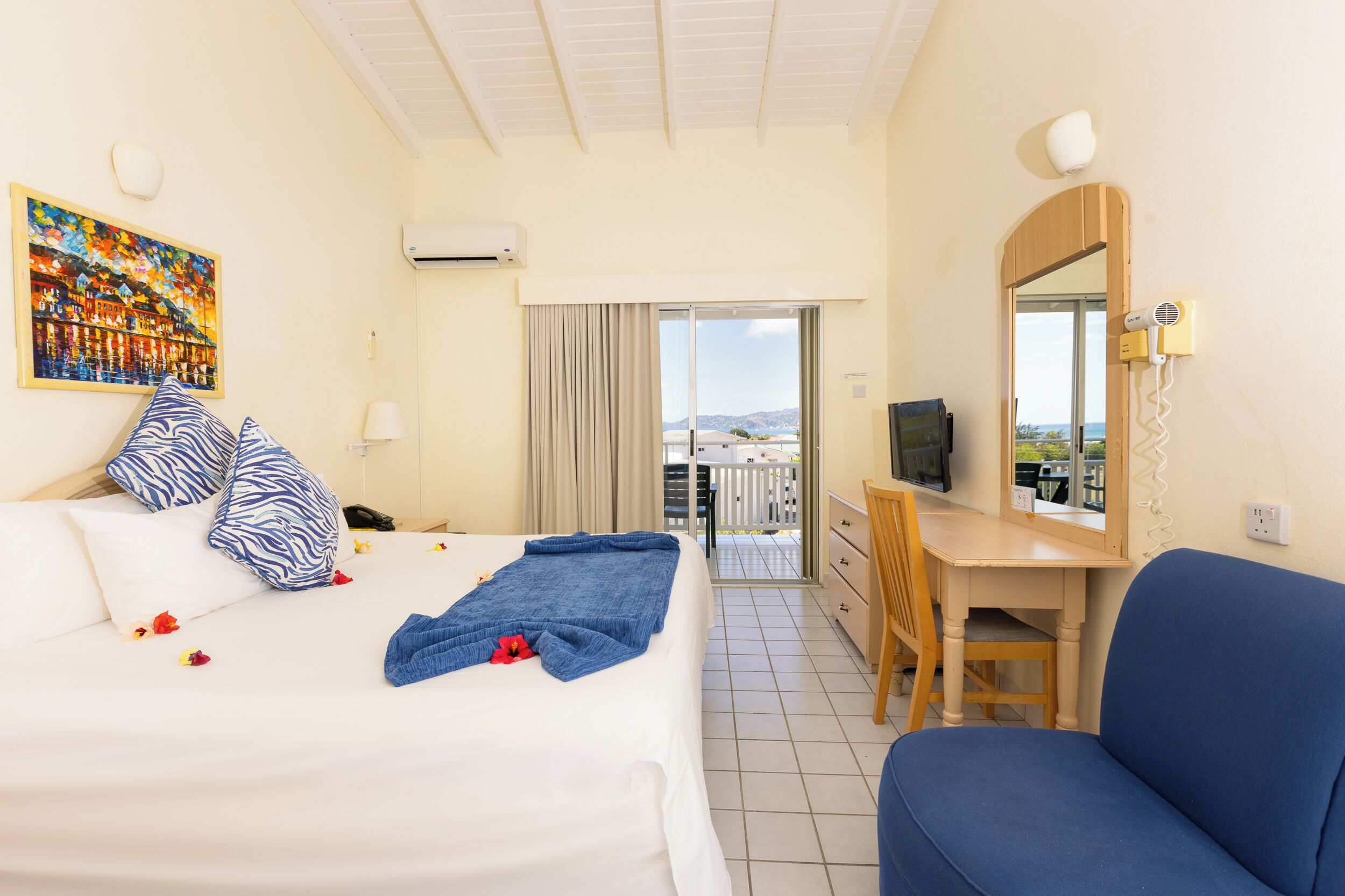 Ett hotellrum med en säng, ett skrivbord, en stol, en TV och en balkong med utsikt.