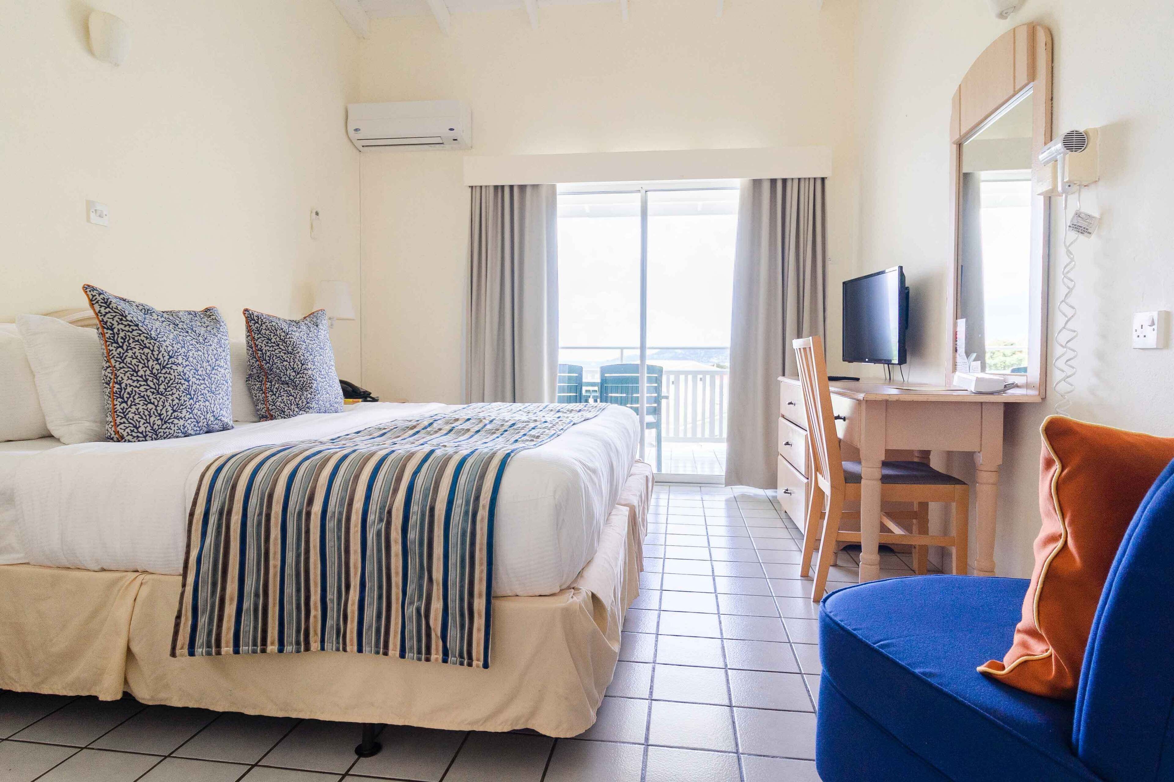 Habitación de hotel con cama, escritorio, silla, televisor y vista al balcón.