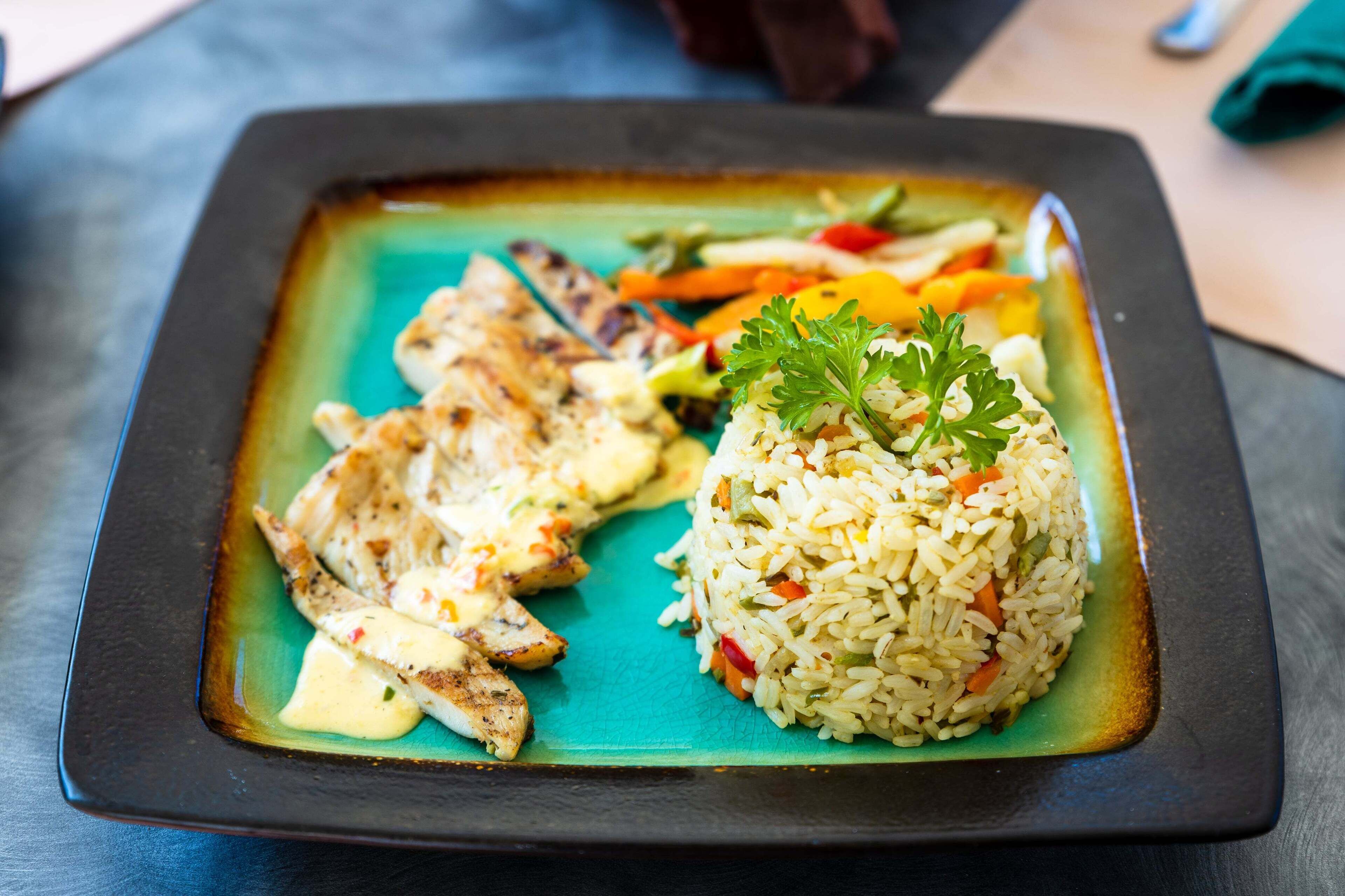 A plate of grilled chicken and rice with vegetables on a teal plate.