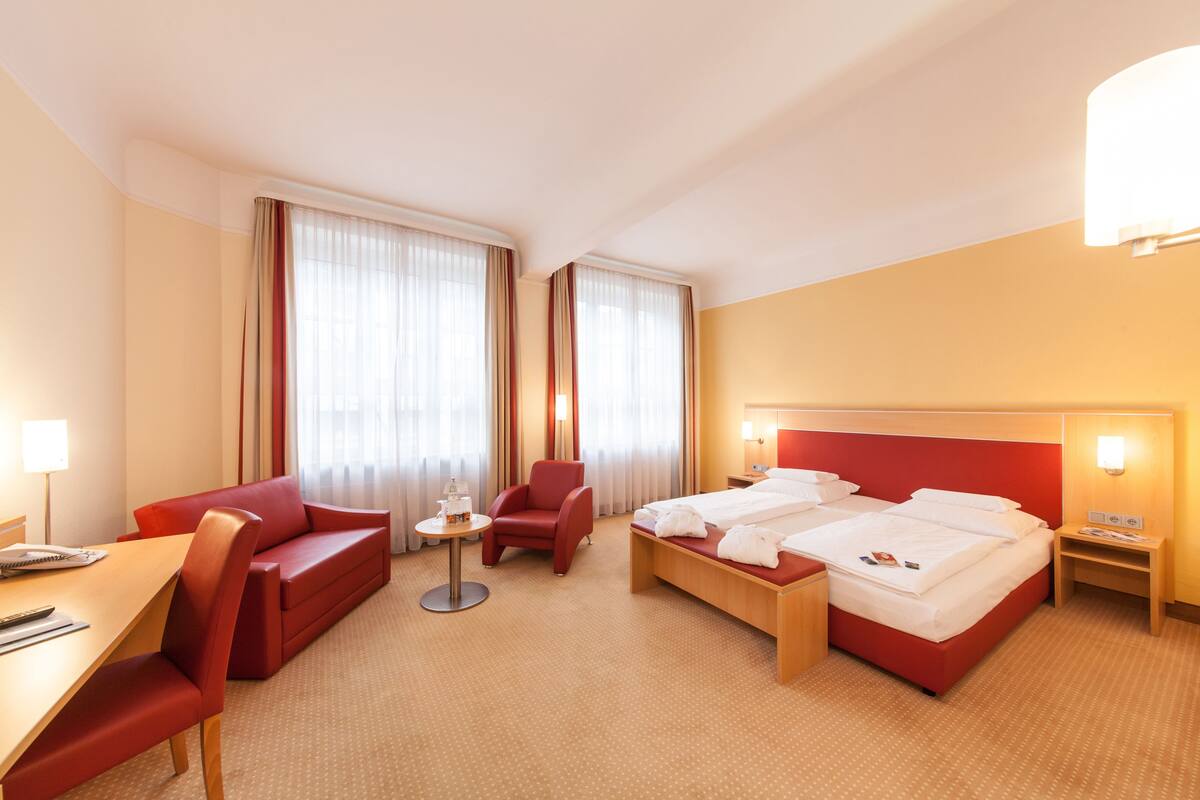 Une chambre d’hôtel avec un lit, un canapé rouge, une petite table et une chaise.