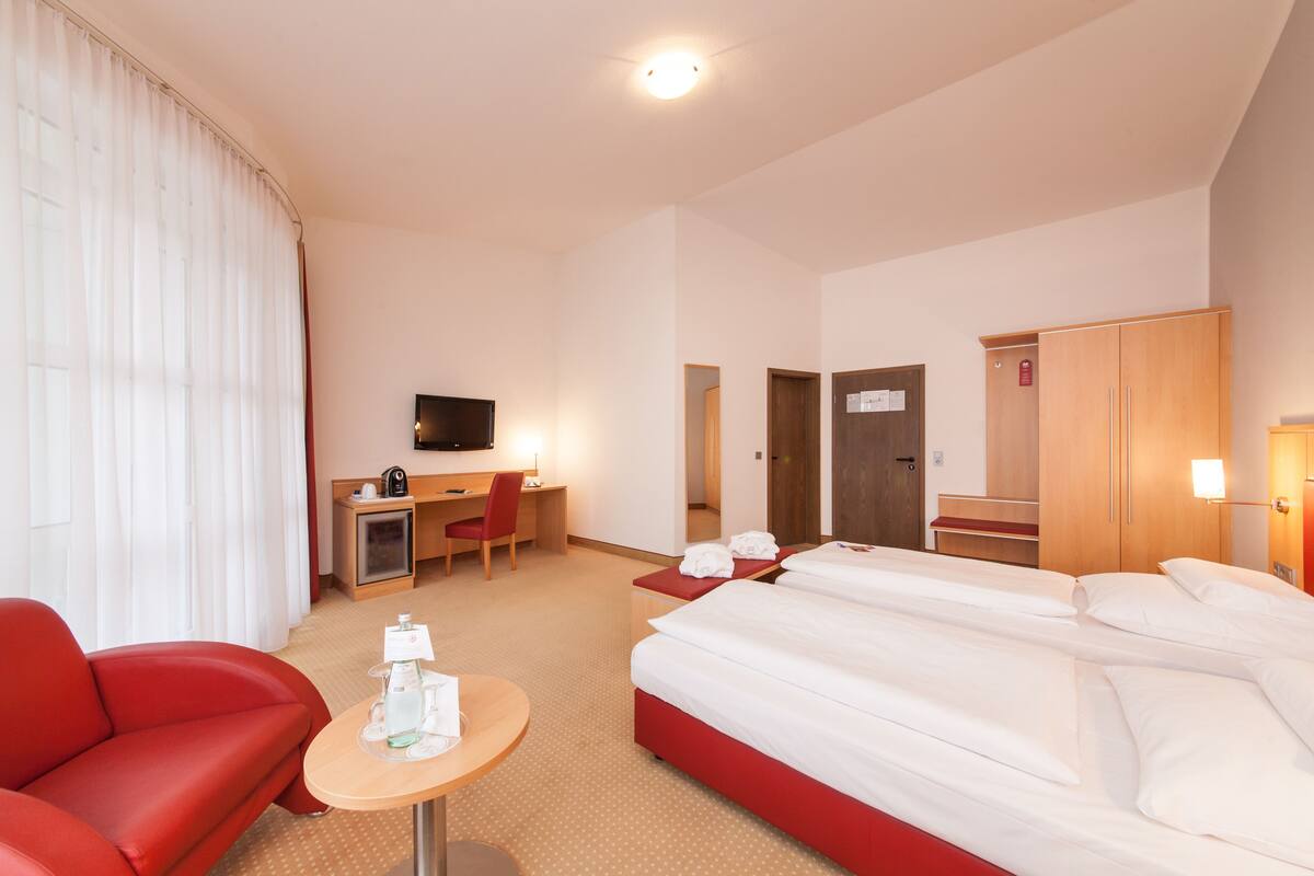 Une chambre d’hôtel avec un lit, un bureau et une chaise, une télévision et un canapé rouge.