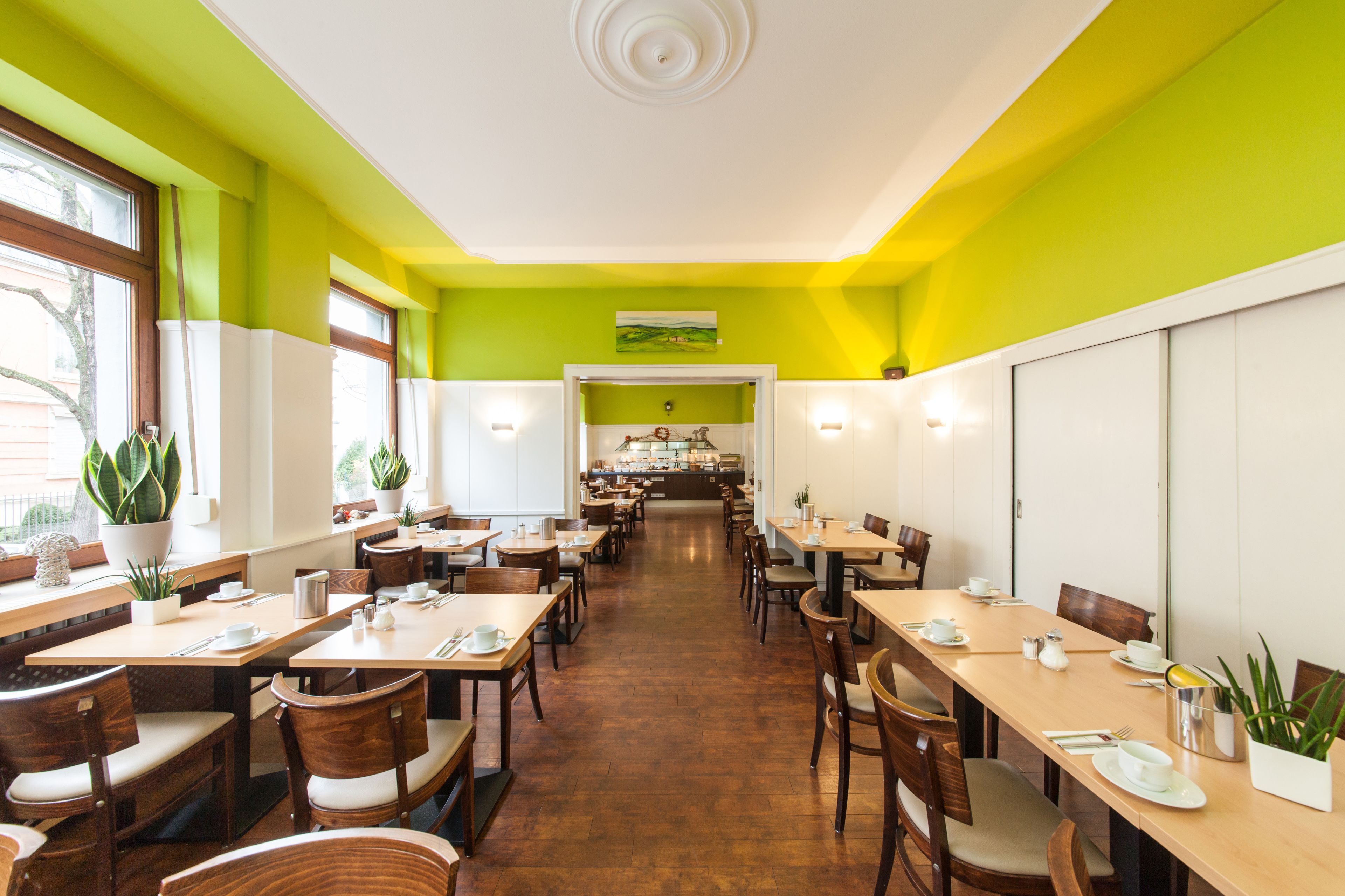 A restaurant with wooden tables and chairs, a kitchen in the background, and green walls.
