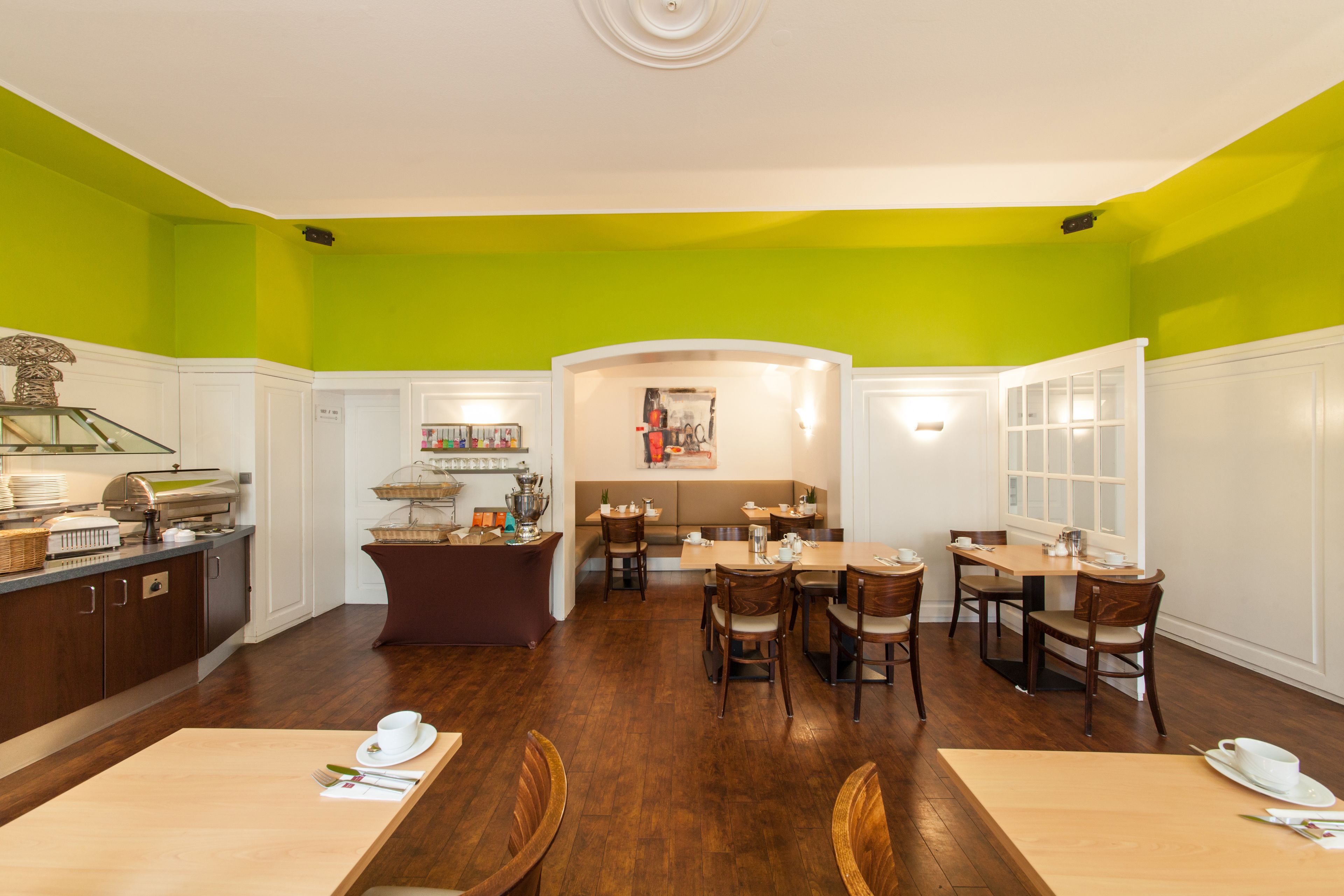 A dining area with wooden tables and chairs, a buffet station, and a kitchen area with white cabinets.