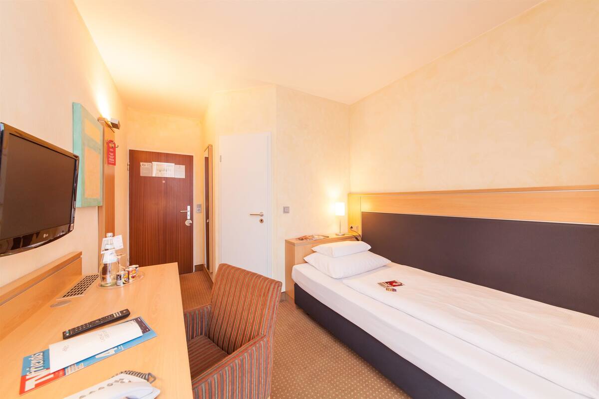 Une chambre d’hôtel équipée d’un lit, d’une télévision, d’un bureau, d’une chaise et d’une table de chevet avec une lampe.