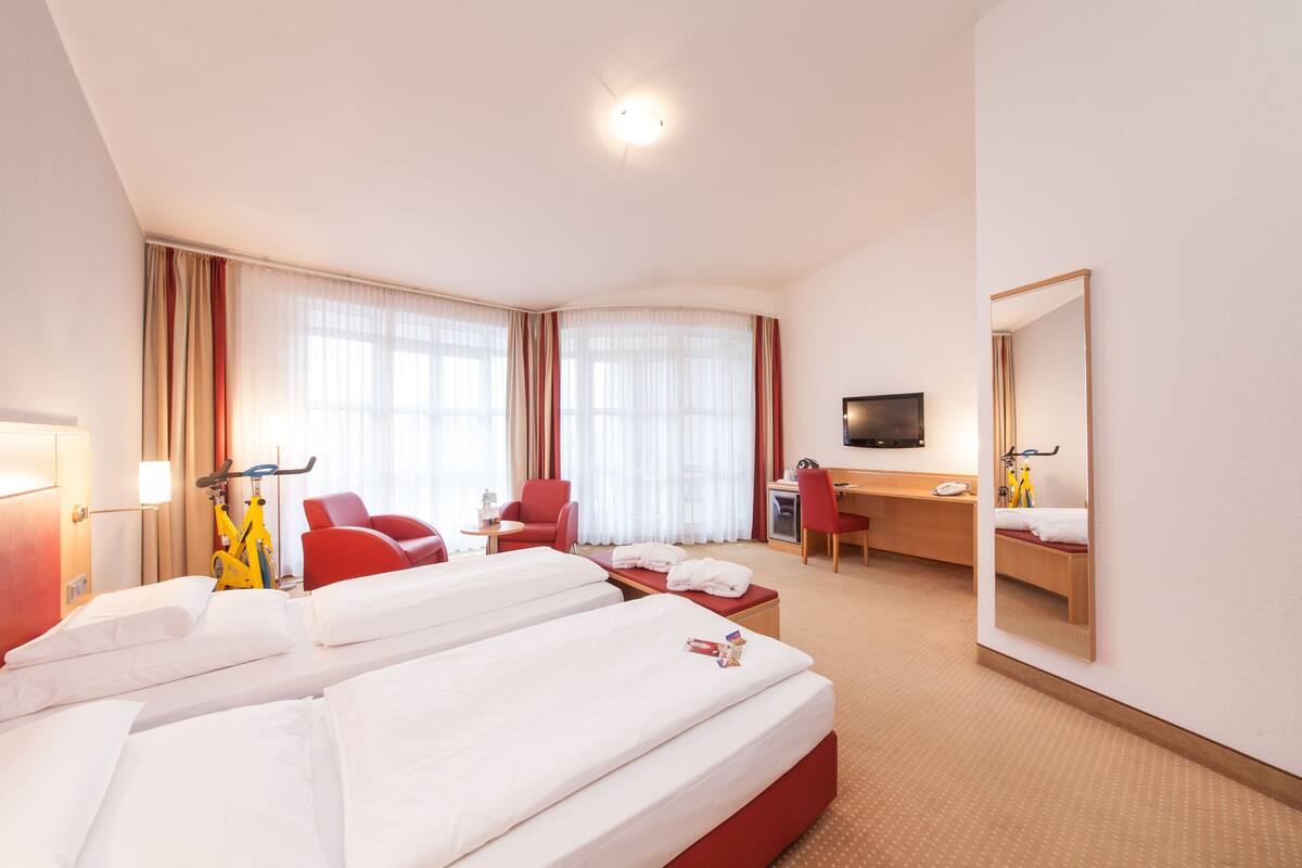Une chambre d’hôtel avec deux lits, un bureau, une chaise, une télévision et un miroir.