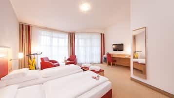 Ein Hotelzimmer mit zwei Betten, einem Schreibtisch, einem Sessel, einem Fernseher und einem Spiegel.