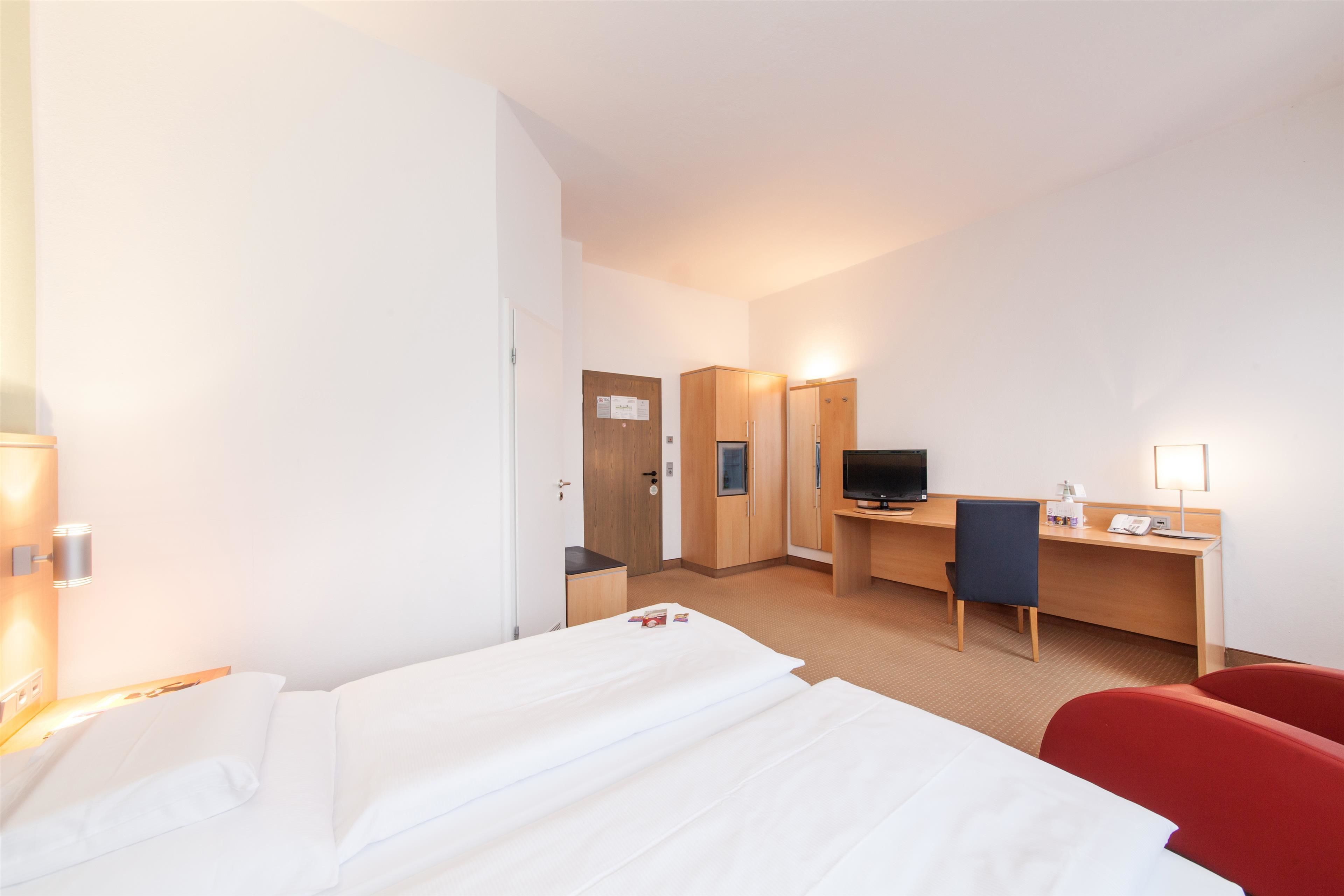 Ein Hotelzimmer mit einem Bett, einem Schreibtisch mit Stuhl, einem Fernseher und einer Schreibtischlampe.