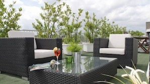 Eine Terrasse mit Korbmöbeln, einem Glastisch und Topfpflanzen.