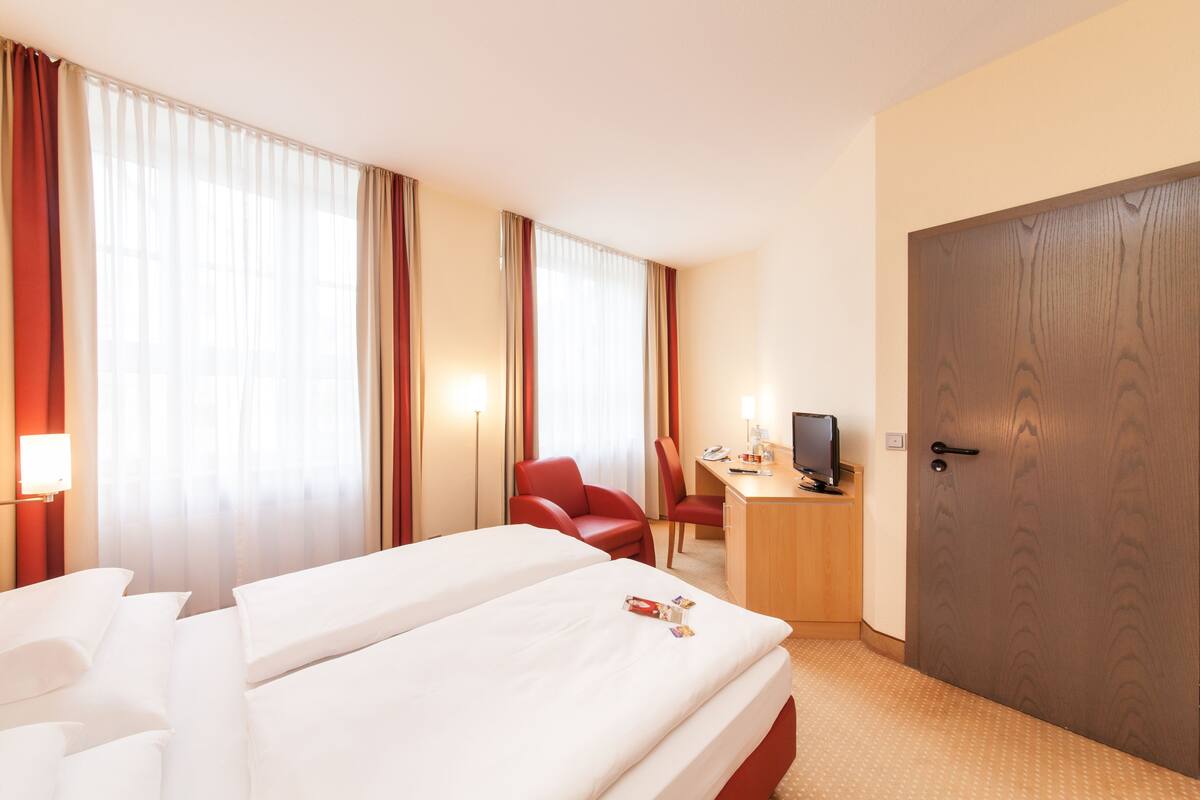 Une chambre d’hôtel avec deux lits, un bureau avec un ordinateur, une chaise et une porte en bois.
