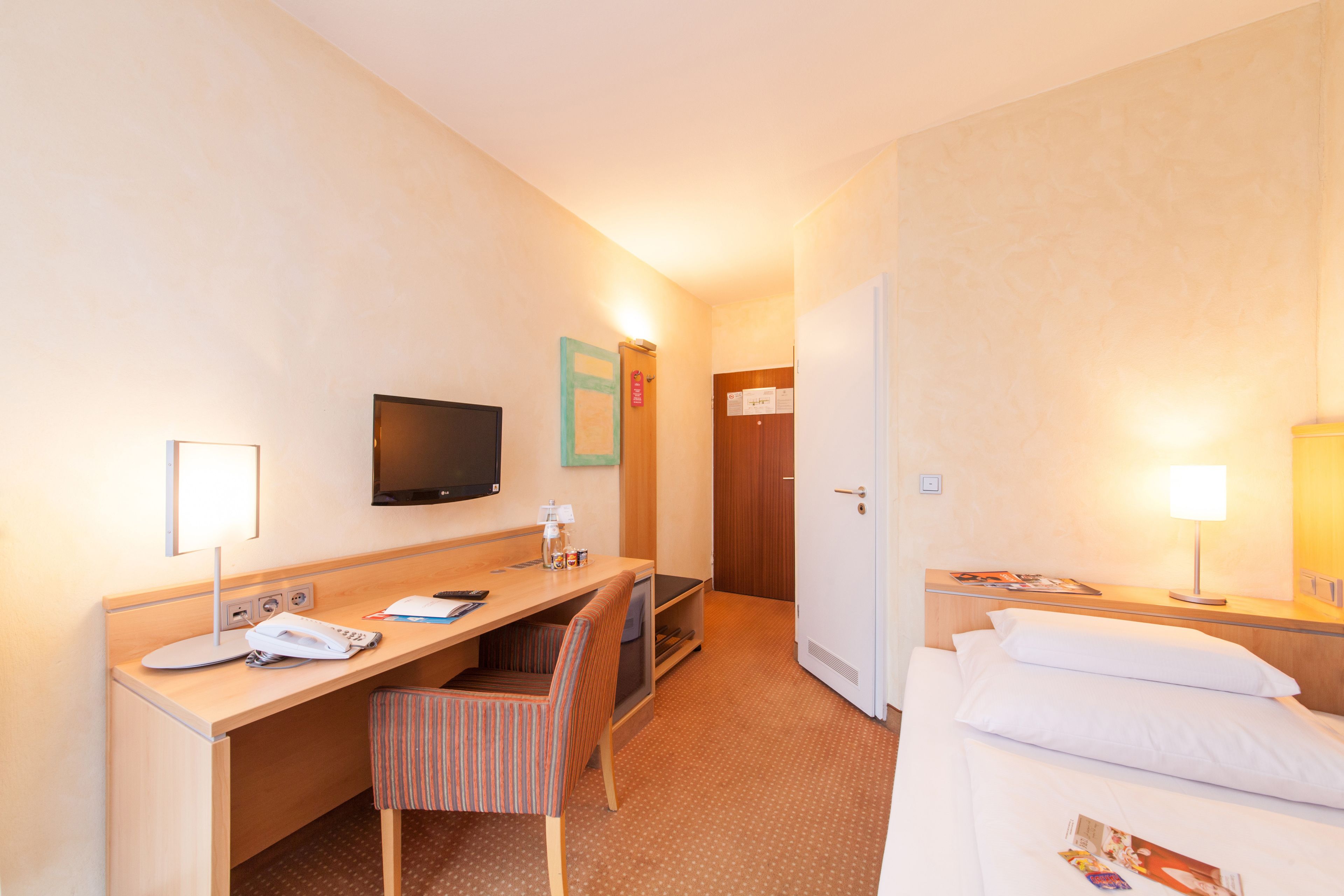 Ein Hotelzimmer mit einem Bett, einem Schreibtisch mit Stuhl, einem Fernseher und einer Tür.