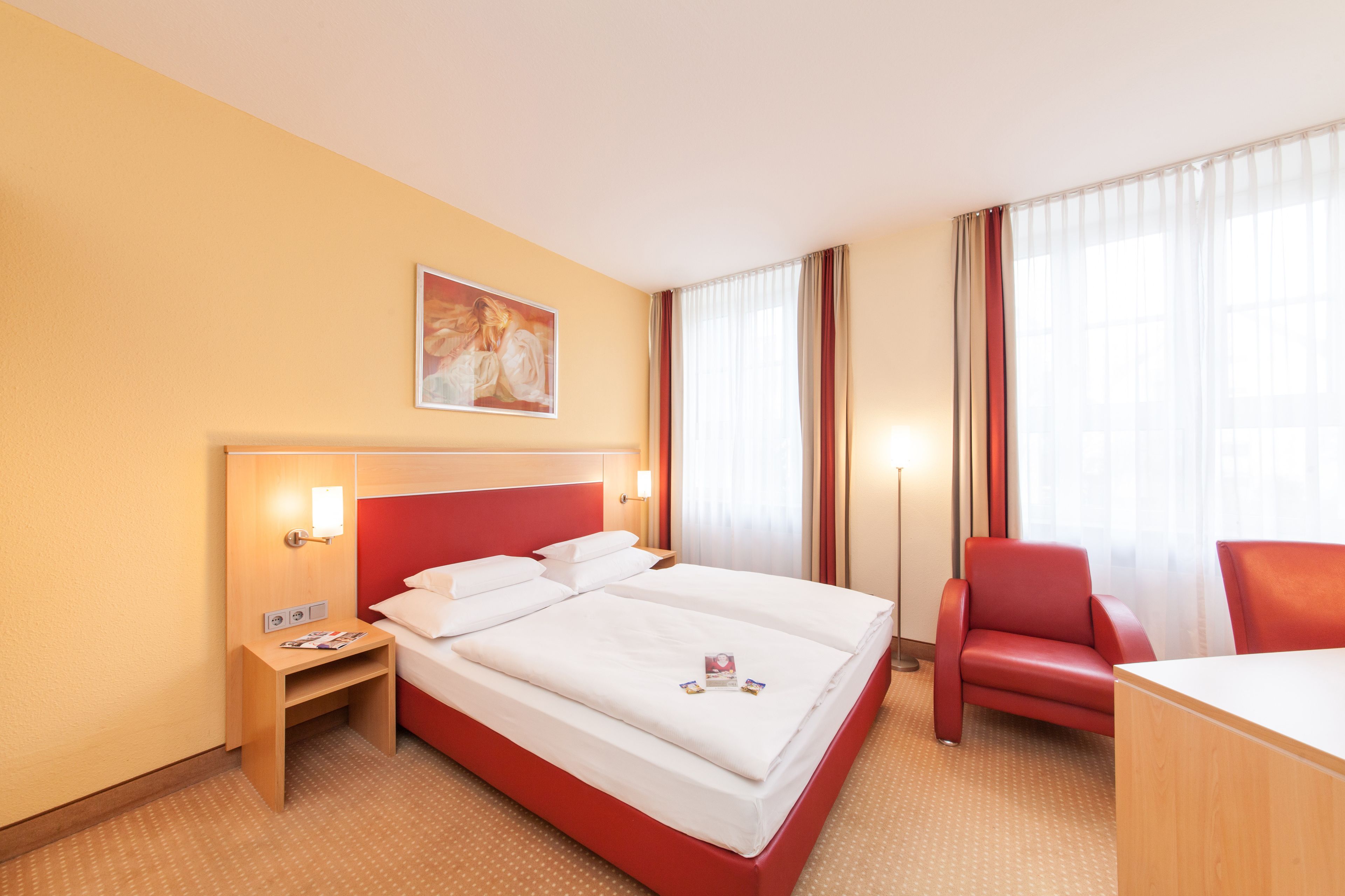 Ein Hotelzimmer mit einem großen Bett, einem Schreibtisch, einem Sessel und einem Bild an der Wand.