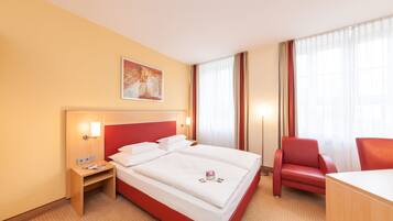 Ein Hotelzimmer mit einem großen Bett, einem Schreibtisch, einem Sessel und einem Bild an der Wand.