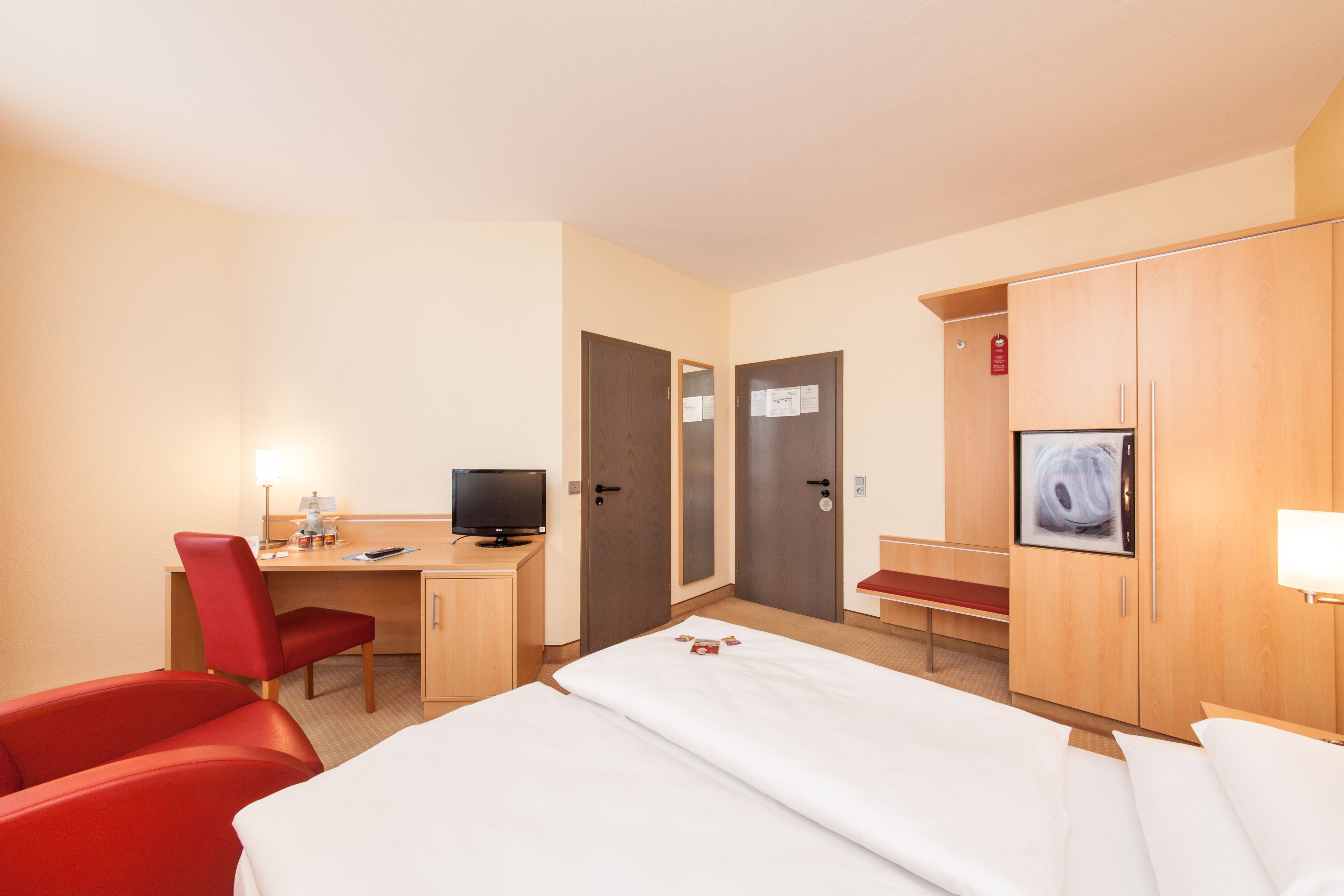 A hotel room with a bed, a desk with a computer, a chair, and a wardrobe.