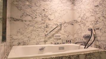 A marble bathroom with a bathtub, a handheld showerhead, and a soap dispenser.