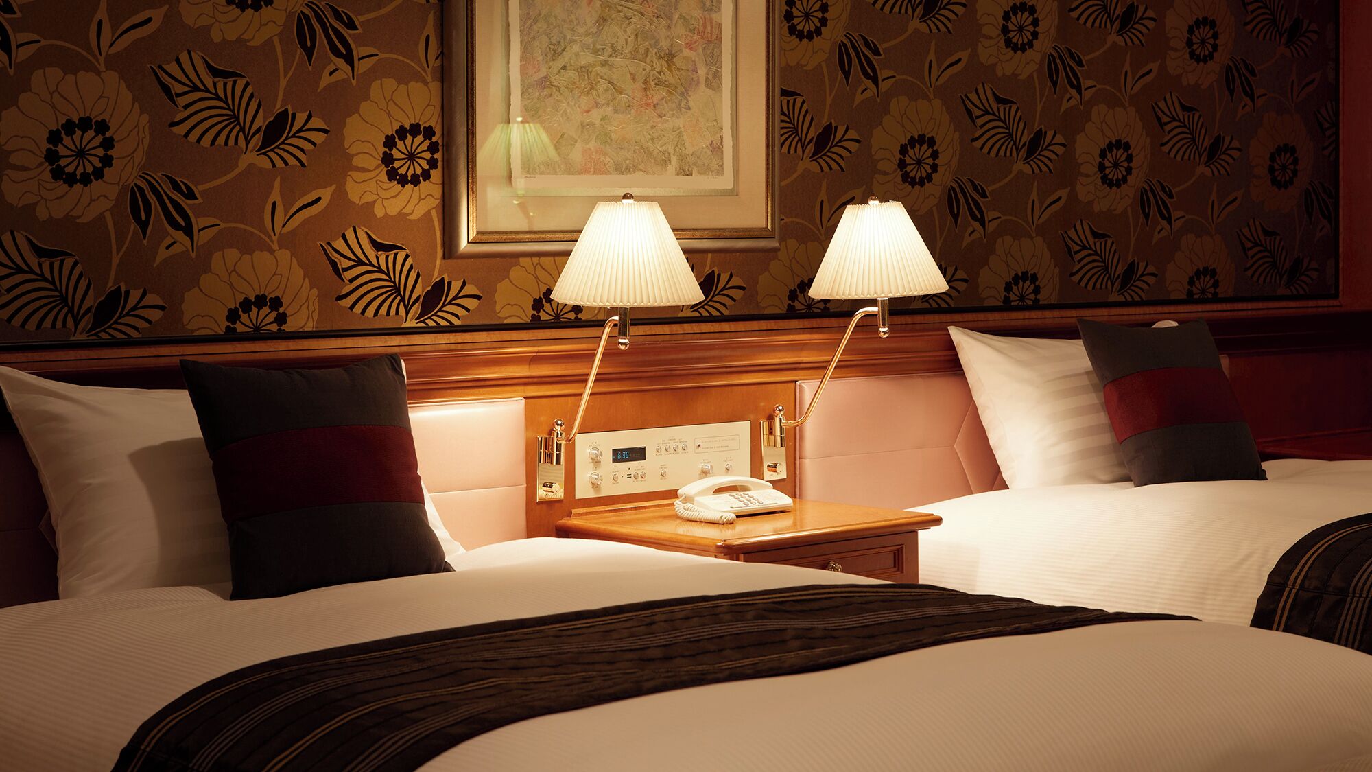 Ein Hotelzimmer mit zwei Betten, einem Nachttisch mit Lampe, einer Uhr und einem Telefon.