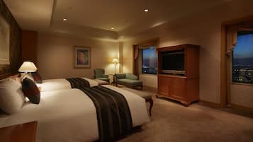 A hotel room with two beds, a television, a desk, and a window with a city view.