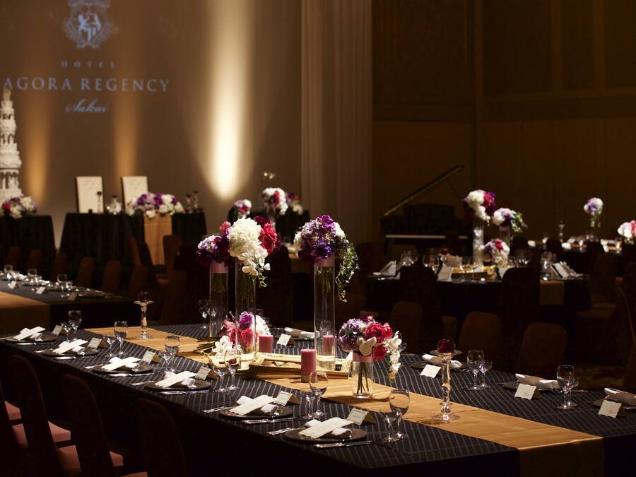 A banquet table set for a formal event with floral centerpieces, name cards, and a projection of the hotel name in the background.