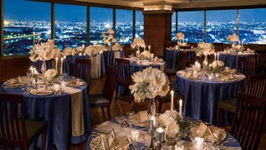 A restaurant with round tables set for dining, featuring blue tablecloths and white floral centerpieces, with a cityscape view through large windows. - Hotel Agora Regency Osaka Sakai (Sakai)