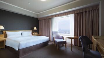 A hotel room with a large bed, two bedside tables with lamps, a chair, a desk, and a view of the city through the window.