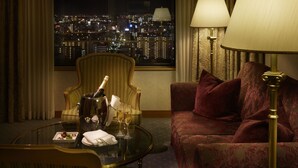 A hotel room with a city view, a glass table with a bottle and glasses, a patterned sofa, and a lamp. - Hotel Agora Regency Osaka Sakai (Sakai)