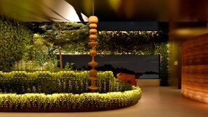 Un interno moderno con una scultura centrale in legno, pareti verdeggianti e un'ampia televisione a schermo piatto.